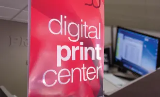 Sign reading digital print center on a red background with a blurred office setting